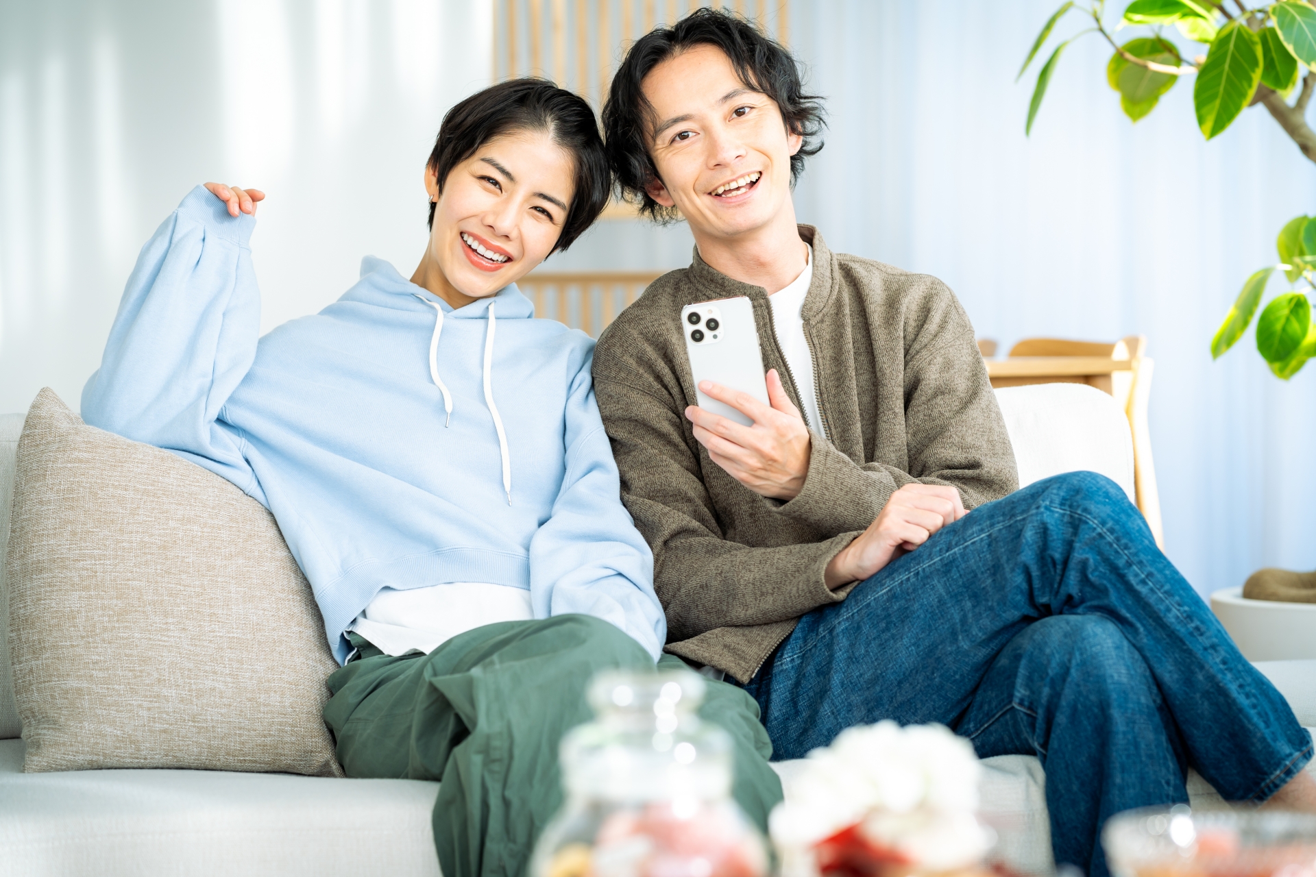 女性が頼れるパートナーのイメージ画像　若い夫婦がソファでくつろいでいる。